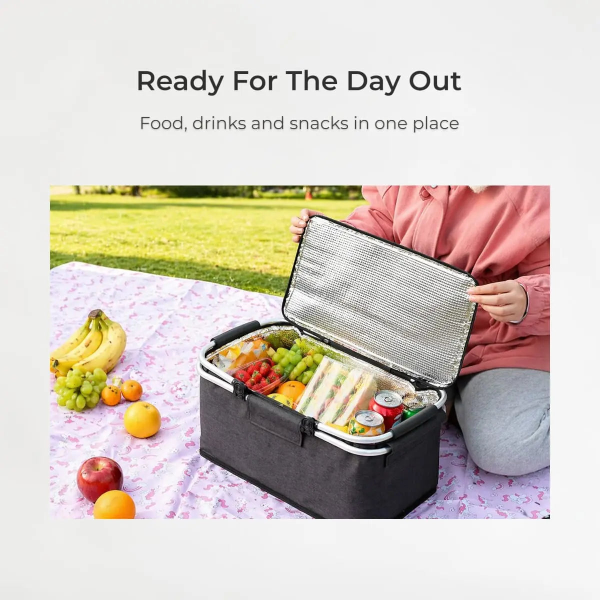 Person holding an open cooler bag with food and drinks on a picnic blanket outdoors.